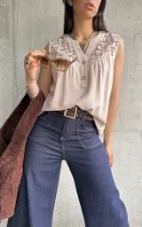 Blusa beige sin mangas con detalle de encaje en el cuello y botones en el frente.