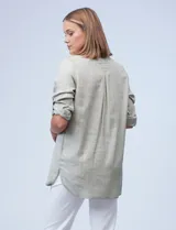 Camisa verde claro con finas líneas verticales blancas, de tencel, con cuello con solapa y abertura central con botones. Tiene dos bolsillos frontales con solapa y botón. Las mangas son largas y regulables con presilla y botón.