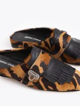 Mocasines destalonados tipo slide confeccionados en cuero vacuno con pelo en estampado animal print, con detalles en cuero negro, flecos frontales y un cierre metálico de torniquete.