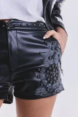 Short negro de cuero sintético, tiro bajo, con tachas y bordado floral en el lateral.