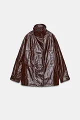 Chaqueta amplia de efecto piel en color marrón oscuro, con cuello alto, manga larga y bolsillos delanteros. Presenta cintura ajustable, forro interior y cierre frontal con cremallera y botones ocultos por solapa.