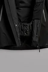 Cazadora deportiva de esquí en color negro, confeccionada en tejido técnico impermeable de tres capas con costuras y cremalleras termoselladas. Cuenta con capucha ajustable, ventilación en axilas, puños con ajuste de tira adherente y puño interior elástico con abertura para el pulgar. Incluye sistema de rescate RECCO y faldón interior para protección contra el frío.