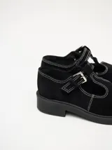 Zapatos tipo guillermina de gamuza color bordó, con diseño de tira en T, cierre con hebilla metálica y costuras a la vista en hilo blanco. Poseen una suela de plataforma de goma negra de 4 cm.