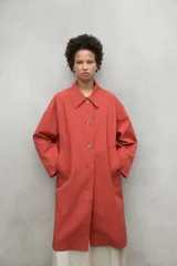 Chaqueta larga de corte holgado en color terracota, con cuello camisero, cierre frontal de botones y bolsillos laterales. Es una prenda repelente al agua, ideal para días de lluvia.