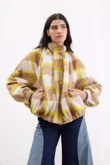 Campera bomber de paño italiano con diseño a cuadros en tonos beige, blanco y amarillo. Presenta un corte oversize, cuello alto, mangas murciélago y cierre frontal con botones a presión.