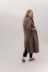 Tapado largo de algodón color marrón oscuro o ciruela, con cuello solapa y mangas largas. Presenta detalles de costuras horizontales que dividen el cuerpo de la prenda y aberturas laterales en el ruedo.