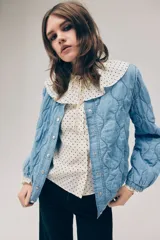 Campera acolchada ligera de denim en mezcla de algodón y lyocell, modelo Divided de H&M. Presenta cuello redondo, cierre frontal con botones a presión, hombros ligeramente caídos, mangas abullonadas y elástico revestido en los puños y el dobladillo inferior. Diseño pespunteado con ondas.