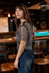 Top de red con brillo metalizado, de corte recto y manga corta. Presenta un diseño translúcido con acabado brillante, ideal para superponer sobre otras prendas.