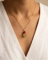 Collar de cadena fina dorada con dije de bronce que combina una piedra roja superior y una estructura esferoide inferior texturizada y calada.