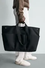 Bolso shopper negro fabricado en tejido técnico, con compartimento principal con cierre de botón a presión, múltiples bolsillos exteriores frontales, doble asa de mano y asas largas de hombro.