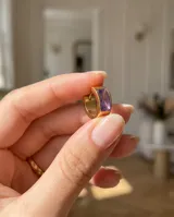 Aros tipo argolla pequeña de acero con baño de oro, con diseño de medio aro y circonia rectangular color violeta.