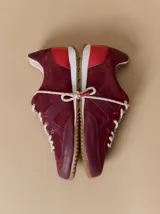 Championes de cuero en tonos bordó y rojo, con diseño de paneles combinados en gamuza y cuero texturizado. Presentan suela blanca con base dentada color caramelo y cordones jaspeados.