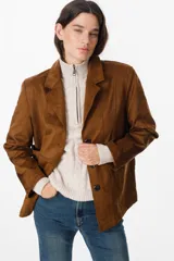 Chaqueta de gamuza sintética color marrón, con solapas clásicas, cierre frontal de botones y bolsillos laterales. Presenta un corte recto y estructurado.