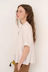 Camisa de manga corta color blanco con cuello mao y cierre frontal de botones. Presenta detalles bordados tono sobre tono en el canesú y diseño de corte recto.