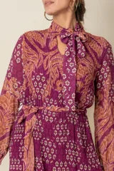 Vestido midi plisado de gasa estampada en tonos violeta y naranja, con lazo en el cuello y en la cintura.