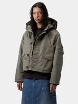 Chaqueta corta tipo bomber con capucha, color verde militar, con cierre frontal de cremallera y botones, bolsillos laterales con solapa y bolsillo utilitario en la manga.