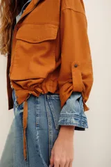 Campera tostado de estilo utilitario, con cuello alto, cierre frontal y bolsillos frontales con solapa. Presenta mangas largas con presillas.