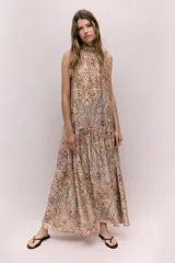 Vestido largo sin mangas, con cuello alto y abertura en la nuca. Presenta un estampado paisley en tonos tierra, rosados y celestes, con frunces a la altura de la cadera que generan una falda acampanada con vuelo.