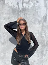 Remera de encaje negro con diseño cruzado frontal y lazo lateral para ajustar. Presenta mangas largas con terminación acampanada y un delicado patrón de pequeñas flores bordadas en toda la prenda.