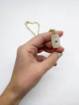 Collar con cadena dorada de eslabones y un dije rectangular de piedra translúcida con detalle circular incrustado en el centro.