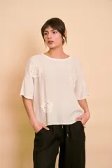 Blusa holgada color beige con mangas cortas y cuello redondo. Presenta apliques bordados con detalles de perlas y lentejuelas en el frente.