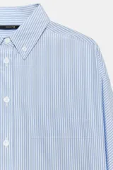 Camisa de manga larga con patrón de rayas verticales en tonos celeste y blanco, cuello con solapa abotonada y un bolsillo aplicado en el pecho. Cierre frontal con botones blancos.