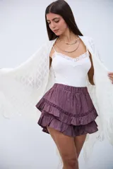 Short pollera de tiro alto con cintura elástica, confeccionado en tela con textura arrugada. Presenta un diseño de dos volados superpuestos con detalles de encaje calado en las costuras.