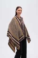 Poncho de tejido grueso con cierre frontal parcial. Presenta un diseño geométrico con bloques de color y patrones a cuadros en tonos marrón oscuro, mostaza, gris y beige.