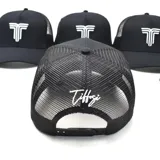 Gorra tipo trucker color negro, con panel frontal rígido y parte trasera de malla. Presenta un logo bordado en relieve de color blanco en el frente.
