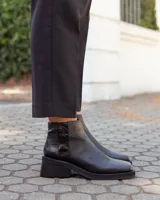 Botinetas de cuero negro con diseño de caña baja y puntera cuadrada. Presentan un panel trasero con textura tipo reptil y un taco bloque bajo de estilo moderno.