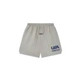 Short de felpa color gris claro, de corte holgado, con cintura elástica y cordón de ajuste largo. Cuenta con un pequeño parche rectangular en la parte superior y la inscripción "USA ESSENTIALS" estampada en azul marino en la pierna izquierda.