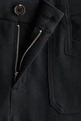 Pantalón amplio de sarga de algodón negro, con perneras rectas, bolsillos delanteros de parche y cierre frontal con botón.