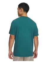 Remera de manga corta Under Armour color verde petróleo, con estampado frontal del logo y nombre de la marca en tono metalizado sobre una franja horizontal. Confeccionada en tejido Charged Cotton de secado rápido y elástico.