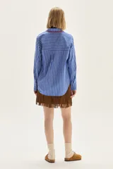 Camisa de corte holgado con diseño de rayas verticales en azul y blanco. Presenta cuello clásico y cartera frontal con detalles bordados en hilo rojo. Incluye un pequeño bordado de estrellas en el pecho y mangas largas con puños estructurados.