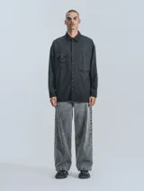 Camisa de manga larga estilo técnico, color negro, con corte oversize. Presenta múltiples bolsillos frontales con solapa y cierre, y un bolsillo adicional en la parte inferior de la espalda. Confeccionada en microfibra suave.