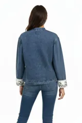 Campera de jean azul con cuello mao y cierre frontal mediante nudos decorativos. Presenta mangas largas con puños vueltos en color blanco con bordados florales y bolsillos frontales tipo parche.