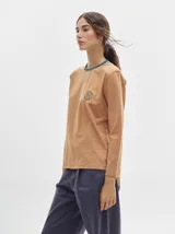 Remera de manga larga con cuello redondo y estampado a rayas horizontales en tonos marrón y negro. Tiene un logo bordado en el pecho de color rojo.