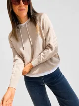 Buzo tejido estilo hoodie de punto, color beige, con capucha y cordones ajustables. Presenta un diseño de manga larga con puños acanalados y un calce cómodo.