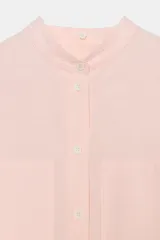 Camisa de corte oversize color rosa claro con diseño de rayas verticales sutiles. Presenta cuello solapa desmontable, cierre frontal con botones ocultos bajo solapa, mangas largas con puños y bajo asimétrico redondeado. Incluye dos bolsillos frontales amplios.