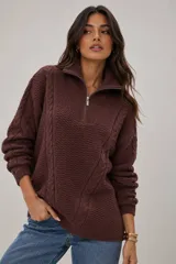 Sweater de punto grueso color marrón, con diseño de trenzas y textura, cuello alto con cierre metálico frontal y calce holgado.