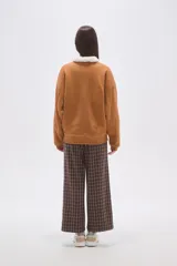 Buzo de algodón color tostado, con cuello polo y cierre frontal parcial con botones. Presenta un detalle de forro de corderito sintético blanco en el cuello y mangas largas con diseño holgado.