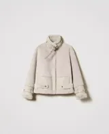 Chaqueta color beige de napa y piel sintética con cuello con cierre de hebilla y almeja, mangas largas con hombros caídos, tirantes en los puños, cierre de cremallera oculta, bolsillos laterales, cierre de hebilla y almeja en el dobladillo y placa en T ovalada en la parte posterior.