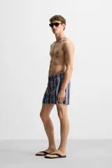 Short de baño confeccionado en tejido técnico con diseño de rayas verticales en tonos azul, marrón y beige. Cuenta con cintura elástica ajustable con cordón, bolsillos laterales y forro interior.