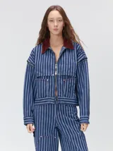 Campera de denim a rayas verticales con cuello de pana en color bordó. Presenta cierre frontal, mangas desmontables con cierre en los hombros, canesú en el pecho y bolsillos de parche cuadrados.