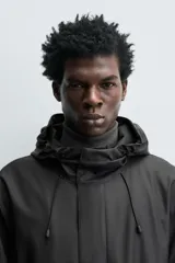 Parka de tejido con acabado engomado, diseño de corte recto y largo medio. Presenta cuello subido con capucha ajustable, cierre frontal con cremallera oculta bajo solapa con botones a presión, mangas largas y bolsillos laterales de vivo.