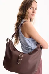 Cartera tipo bolso hobo de cuero sintético negro con textura granulada, asa de hombro ajustable y detalle de tira frontal con hebilla metálica plateada. Cierre superior con cremallera.