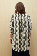Vestido camisero de corte relajado con estampado de ondas verticales en tonos neutros. Presenta cuello clásico, cierre frontal con botones y mangas largas. Confeccionado en tejido fluido con caída liviana.