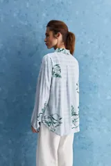 Camisa de calce relajado con cuello clásico, mangas largas con puños elastizados y rayas verticales que aportan un estilo atemporal. Su diseño liviano y versátil cuenta con estampado floral verde sobre fondo de rayas celestes y blancas.