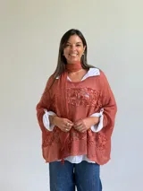 Sweater de punto color naranja con diseño holgado, que incorpora franjas horizontales de encaje con motivos florales. Presenta mangas tres cuartos con puños abotonados y se complementa con una bufanda del mismo tejido y color.