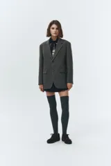 Blazer de lana color gris oscuro, con cuello sastre, cierre frontal de dos botones y hombreras. Presenta parches de ante sintético en los codos y un calce relajado tipo overfit.